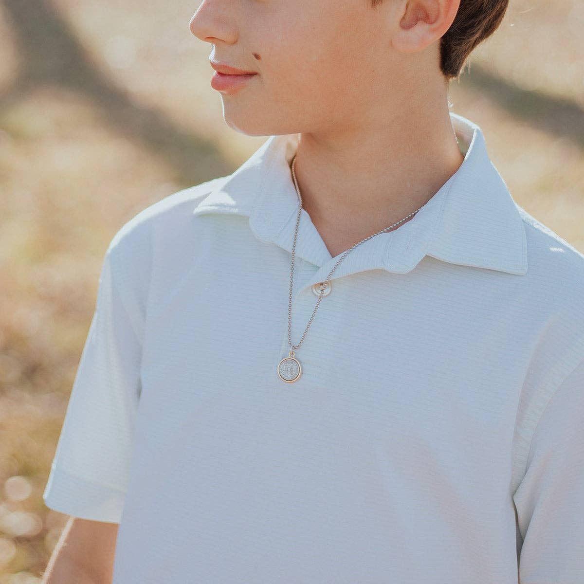 A young boy wearing a white polo shirt and a St. Benedict chain